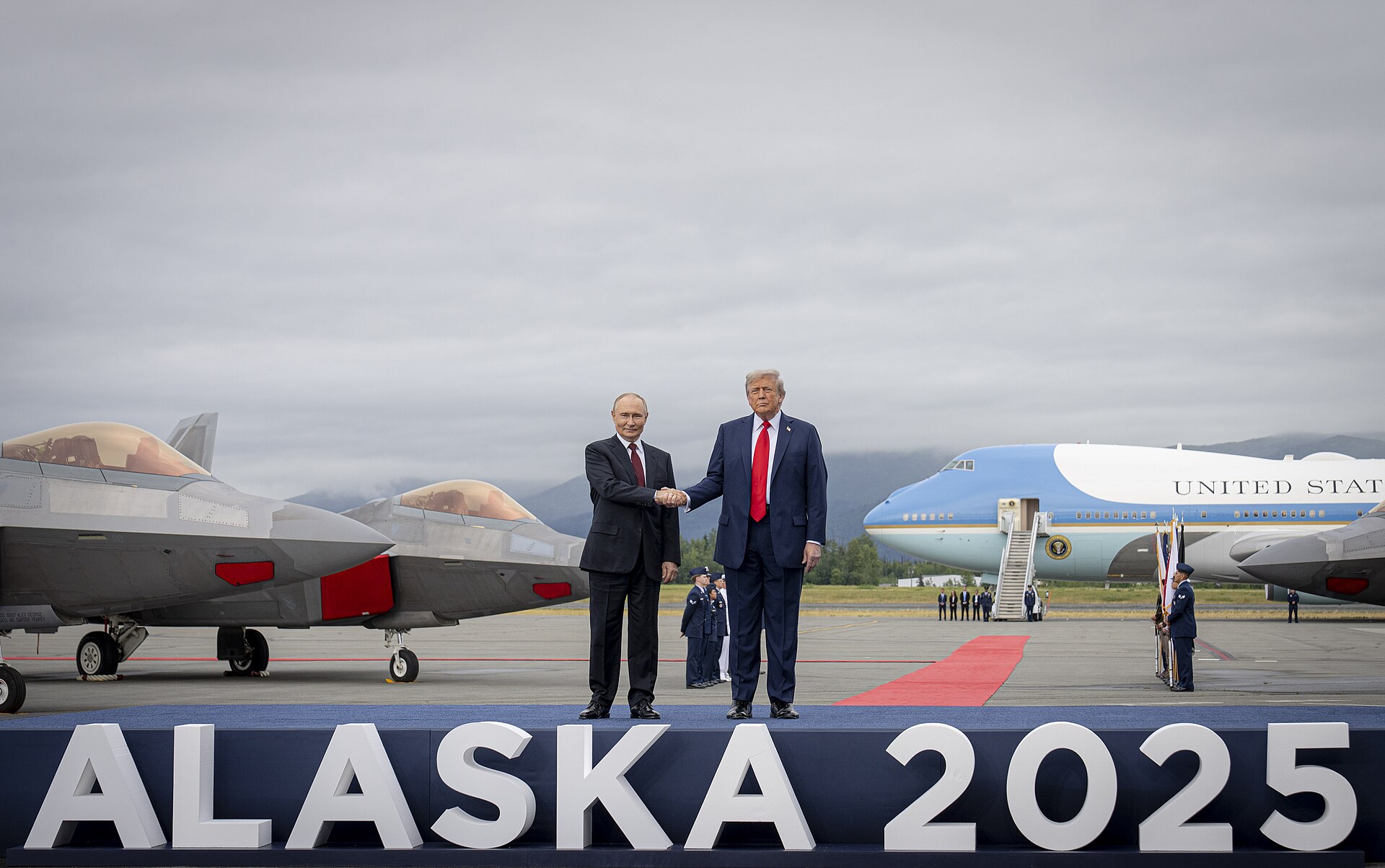 Donald Trump and Vladimir Putin shaking hands on a red carpet at Joint Base Elmendorf-Richardson in Alaska in August 2025
