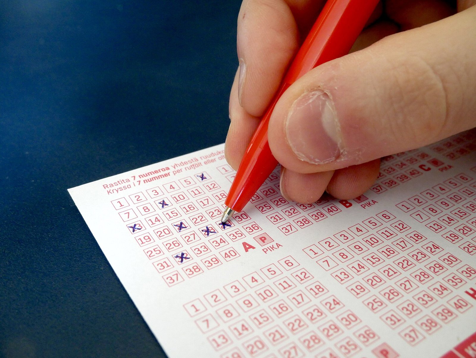 A hand marking numbers on a lottery slip with a red pen